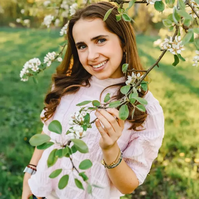 Junge Frau lächelt zwischen weißen Blütenzweigen auf der Streuobstwiese im Frühlingslicht