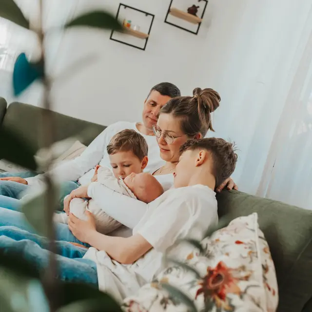 Familie kuschelt auf dem Sofa, der große Bruder hält das neugeborene Geschwisterchen im Arm
